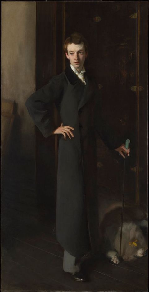 Painting. A full-length portrait of a young man dressed in a long dark coat. One hand rests on his hip while the other holds a cane. He stands on dark wood floorboards and the room behind him is just visible.